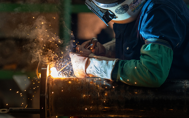 Welder working on metal pipe with sparks flying